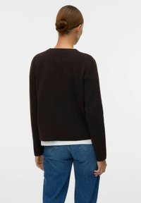 Brauner Strickpullover mit lockerer Passform und Rundhalsausschnitt, kombiniert mit blauen Jeans. Sanfte Textur, einfaches Design.