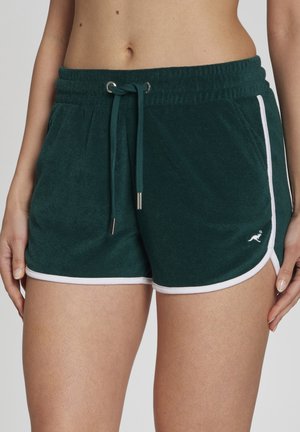 Dunkelgrüne Frottee-Shorts mit weißem Rand und kleinem Känguru-Logo auf der Vorderseite, getragen von einer Person mit den Händen an den Seiten.