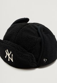 Pălărie de blană neagră tip trapper cu logo-ul New York Yankees și urechi pliabilă, pe un fundal deschis uniform.