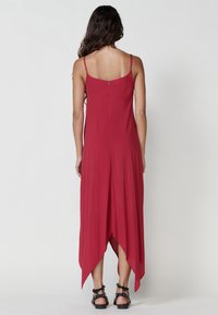 Roter ärmelloser Jumpsuit mit fließendem Design, featuring einem Cutout im unteren Rücken und asymmetrischem Saum. Glattes Material mit weicher Textur.