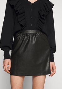 Black sweater with ruffled front detail and button closure, paired with a high-waisted black leather skirt featuring an elastic waistband.