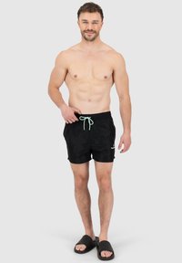 Shorts de bain noirs avec une taille élastique et un cordon de serrage vert menthe. Longueur courte, tissu léger, avec un logo sur l'avant inférieur.