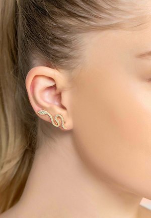Gold-colored ear cuff in a wavy design, embellished with sparkling gemstones. Attached to the earlobe, showcasing a sleek and modern style.