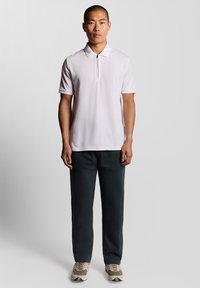 Kortärmad polo skjorta i ljusrosa, med en zip-krage. Matchad med mörkgrå byxor och ljusa sneakers. Enkel design.