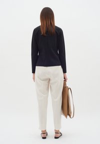 Musthave musta pika varrukatega top, valged kohandatud püksid ja mustad sandaalid, hoides pruuni käekotti. Sile kangas, minimalistlik disain ja neutraalsed värvid.