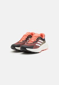 Zapatillas deportivas con un upper de punto rojo y negro, rayas blancas, cordones naranjas y una entresuela blanca en contraste con una suela negra texturizada.