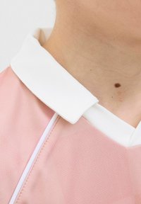 Camisa rosa claro con un cuello blanco. La tela parece suave con una sutil textura y una costura de acento blanca cerca del cuello.