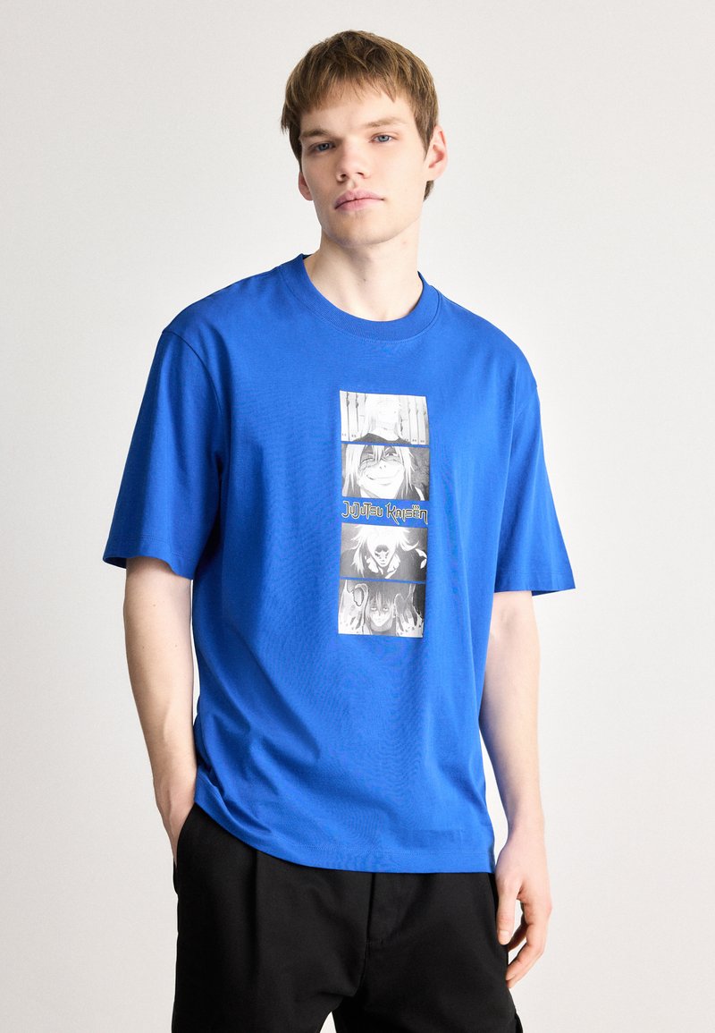 Μπλέ βαμβακερό μπλουζάκι με γραφική εκτύπωση μαύρων και άσπρων χαρακτήρων σε τρία πάνελ, με το κείμενο "Jujutsu Kaisen" σε κίτρινο χρώμα.