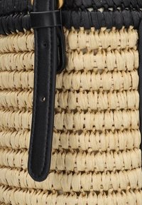 Geweven strooien tas met een mix van natuurlijke beige en zwarte vezels, voorzien van een gladde zwarte leren schouderband en gedetailleerde stikselaccenten.