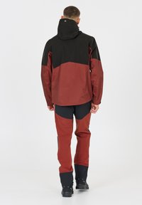 Röd och svart utomhusjacka med huva, har en geometrisk färgblockdesign. Kombinerad med röda byxor och svarta skor. Slät textur.
