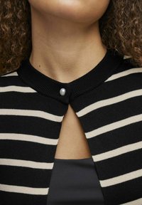 Melna un krēmkrāsas svītrota džemperis ar apaļu kaklu un pērlīšu pogām pie apkakles atvēruma. Redzama gluda izvērsuma struktūra.