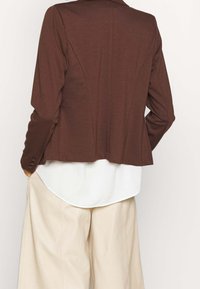 Bryn skräddarsydd jacka med notchkrage, långa ärmar och knapprad. Kombinerad med krämfärgade vida byxor.