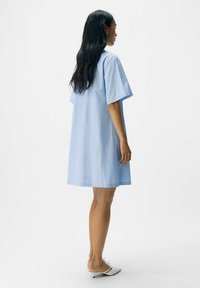 Abito a righe blu chiaro in una vestibilità ampia, maniche corte, che arriva a metà coscia. Tessuto di cotone liscio con dettagli di design minimi.