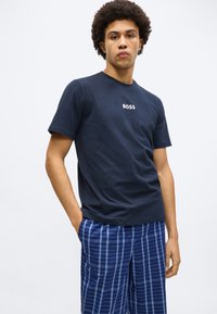 Tricou din bumbac albastru închis cu logo-ul "BOSS" alb, asortat cu pantaloni scurți în carouri albastre, având nuanțe variate de linii albastre.