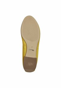 Chaussure plate jaune avec un dessus lisse et une semelle en caoutchouc texturée. Possède un petit talon et un logo de marque visible sur la semelle intérieure.