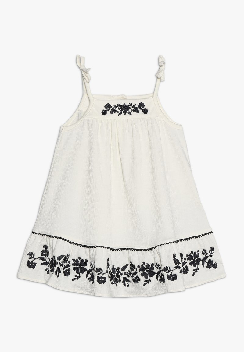 Robe blanche sans manches avec fines bretelles à nouer, broderie florale noire sur la poitrine et l’ourlet, tissu texturé.