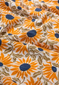 Bavlnená tkanina s kvetinovým vzorom, na ktorej sú oranžové slnečnice s modrými stredmi na smotanovom pozadí. Zelené listy ako akcenty.