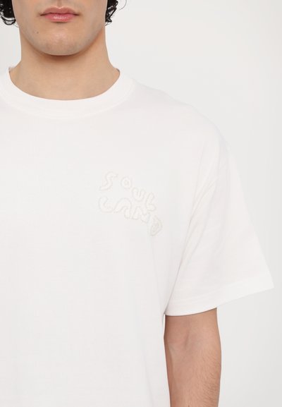 White cotton t-shirt featuring a subtle embroidered "SOUL LAND" logo on the left chest area; short sleeves, round neckline.