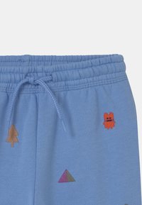 Pantalones de chándal de color azul claro con cinturilla elástica y cordón; presentan patrones bordados de árboles, formas geométricas y un personaje.
