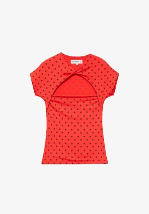 Chemise rouge à manches courtes avec des pois noirs et un détail découpé torsadé au niveau de la poitrine, posée à plat sur un fond blanc.