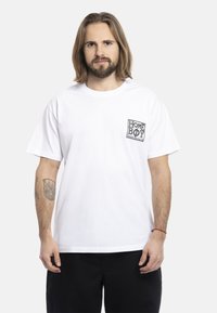 White cotton T-shirt with short sleeves, featuring a black graphic design on the left chest pocket area. Straight cut, relaxed fit.