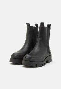 Schwarze Leder-Stiefeletten mit einer klobigen Plateausohle, elastischen Seiteneinsätzen und Anziehlaschen für einfaches Anziehen. Glatte Textur und elegantes Design.