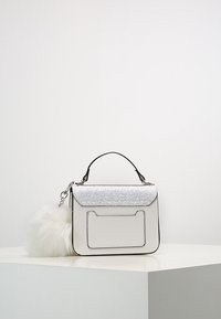 Sac à main blanc avec un rabat argenté scintillant, finition texturée, bord noir, anse supérieure et un accent de pompon en fausse fourrure blanche détachable.