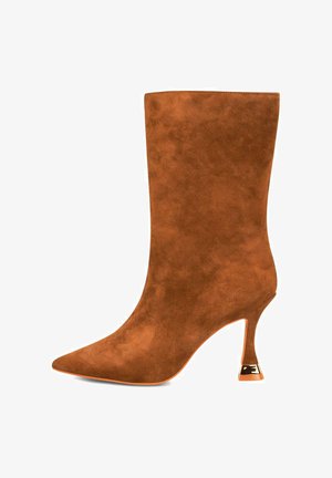 Bottillon en daim brun avec un bout pointu et un talon élégant accentué de doré. Le design est lisse sans motifs ni matériel visible.