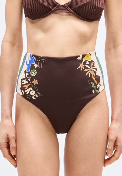 Femme portant un bas de bikini taille haute marron avec des imprimés abstraits et tropicaux colorés sur les côtés, assorti à un haut de bikini côtelé marron.