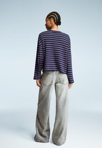 Striped long-sleeve shirt in navy with red and white stripes, paired with oversized light gray jeans. Smooth fabric and relaxed fit.