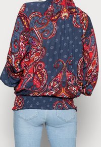 Blusa de color marino con un patrón paisley colorido, que presenta mangas abullonadas y una cintura fruncida para un ajuste relajado. Tejido texturizado con acentos florales.