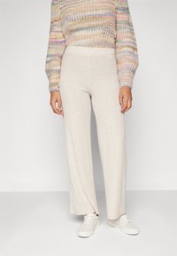 Pantaloni beige a gamba larga realizzati in un tessuto a coste, con una fascia alta in vita e abbinati a sneakers bianche.