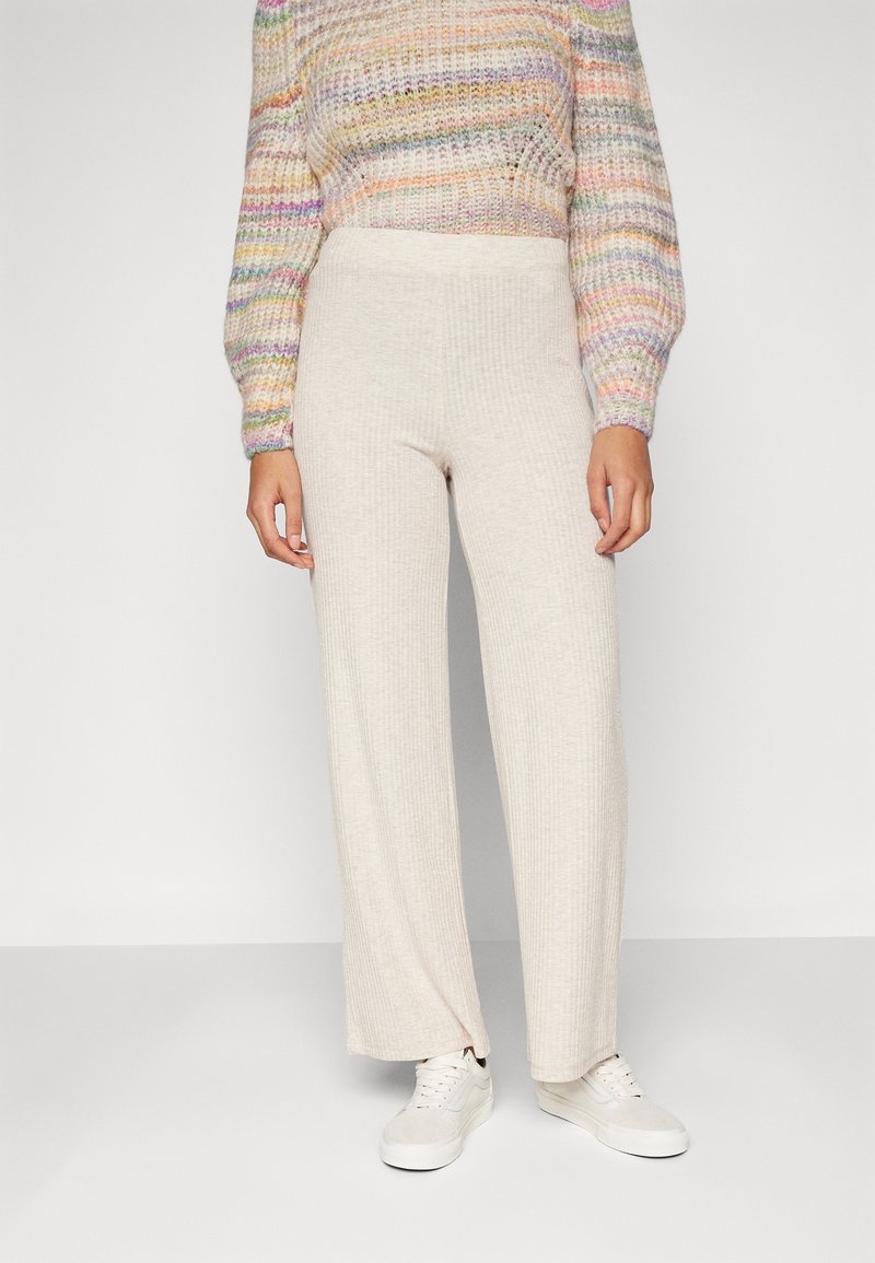 Pantaloni beige a gamba larga realizzati in un tessuto a coste, con una fascia alta in vita e abbinati a sneakers bianche.