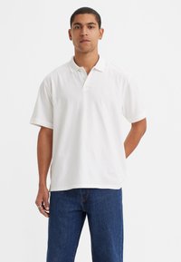 Hvit polo skjorte med korte ermer, krage og en avslappet passform. Brukt sammen med blå denim jeans, som fremhever et uformelt utseende.