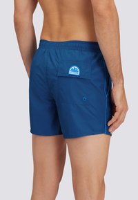 Costume da bagno blu con elastico in vita, taschino posteriore e dettagli azzurri. Realizzato in materiale leggero e ad asciugatura rapida.