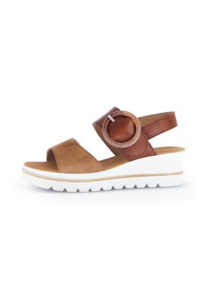 Brown suede sandal with a wide strap and leather accents, featuring a circular hardware detail and a white wedge sole.