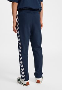 Donkerblauwe sweatpants met een elastische tailleband, met een wit chevronpatroon aan de buitenzijde. Glad stof en taps toelopend ontwerp.
