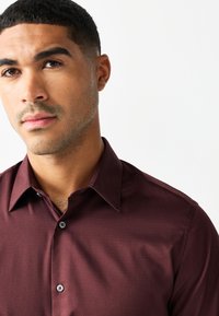Camicia da uomo bordeaux con finitura strutturata, dotata di colletto classico, chiusura con bottoni e silhouette aderente.