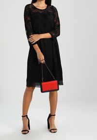 Mustalace mekko, jossa on kolmannen osan hihat, yhdistettynä puna-mustaan laukkua. Ominaisuuksia ovat läpikuultava rakenne, yksinkertainen leikkaus ja korkokengät.