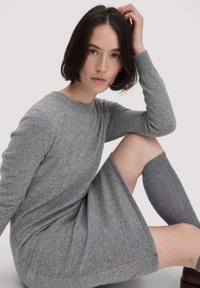 Abito in maglia grigio con scollatura rotonda e maniche lunghe, caratterizzato da una vestibilità morbida. Il modello indossa calze alte fino al ginocchio abbinate con un motivo a coste.