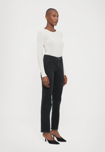 Black jeans with a high waist and a straight cut, paired with a fitted white long-sleeve top and black heeled shoes. Simple design and muted colors.