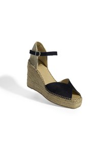 Sandale espadrille compensée en suède noir avec bout ouvert et bride à la cheville. Comprend une semelle en jute tissé et un talon texturé beige.