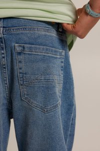 Jeans in denim di un blu chiaro con una tasca posteriore caratterizzata da un design di cucitura angolato e appuntito. Il tessuto presenta una texture sbiadita.