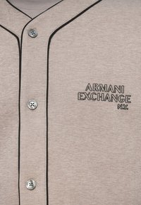 Polo de algodão cinza claro com acabamento em preto, apresentando um botão prateado e o logo bordado "Armani Exchange" no lado esquerdo do peito.