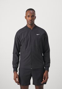 Schwarze Zip-Up-Jacke mit langen Ärmeln, hoher Kragen und Fronttaschen; aus leichtem Stoff, mit kleinem weißen Logo.