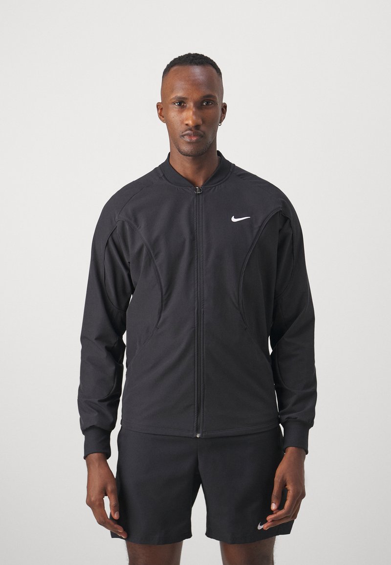 Schwarze Zip-Up-Jacke mit langen Ärmeln, hoher Kragen und Fronttaschen; aus leichtem Stoff, mit kleinem weißen Logo.