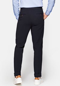 Granatowe spodnie o wąskim kroju, z tylnymi kieszeniami i podwiniętymi mankietami. Materiał wydaje się gładki, a całość dopełniają brązowe akcenty na butach.