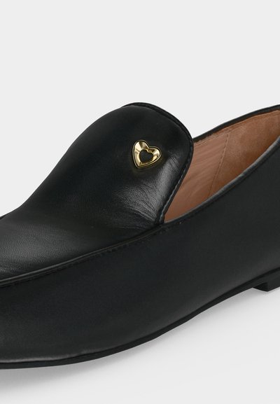 Mocassin en cuir noir avec une petite décoration métallique dorée en forme de cœur sur le dessus, doublure intérieure beige et petit talon.