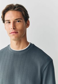 Grå tekstureret sweatshirt med rund krave og lodret ribbet mønster. Har en lagdelt hvid inderskabel.