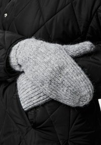 Grå strikkede vanter med en tykk, struktureret vævning og en forlænget manchette, båret over en sort, quiltet jakke. Blød og varm fremtoning.